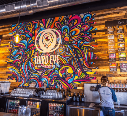 Third Eye Brewing wall with logo and woman pouring beer