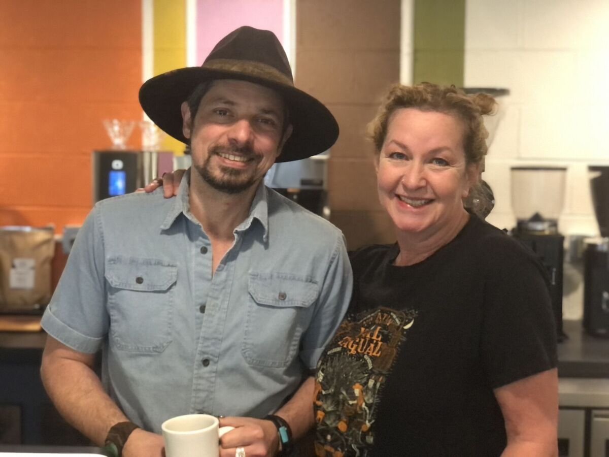 man and woman smiling for photo while man holds coffee